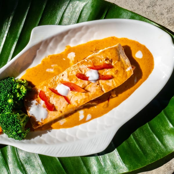 Thailicious salmon in red curry sauce with broccoli, served on a fish-shaped plate over a banana leaf.