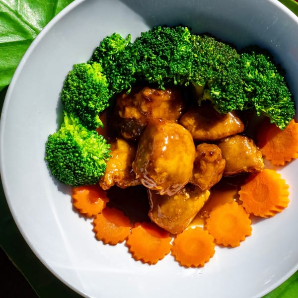 Thailicious' Thai dish with glazed chicken, broccoli florets, and carved carrot slices on a white plate.