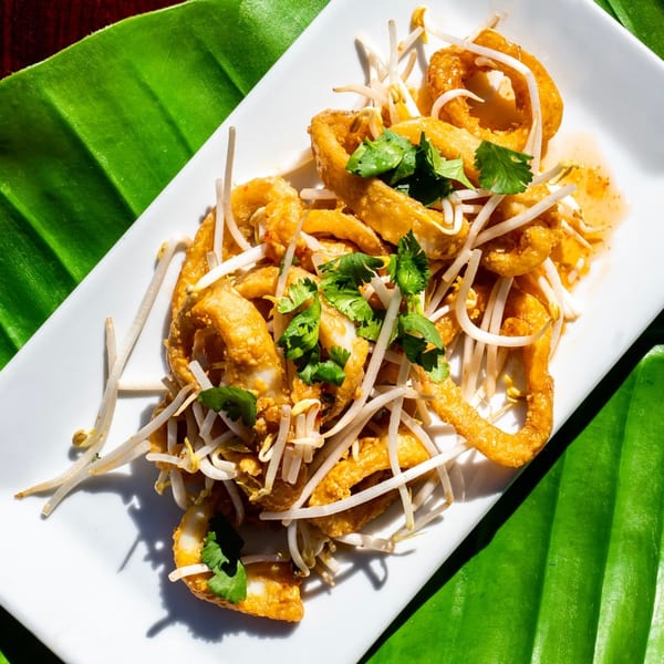 Crispy fried calamari rings with bean sprouts and cilantro on a white plate, on a banana leaf.