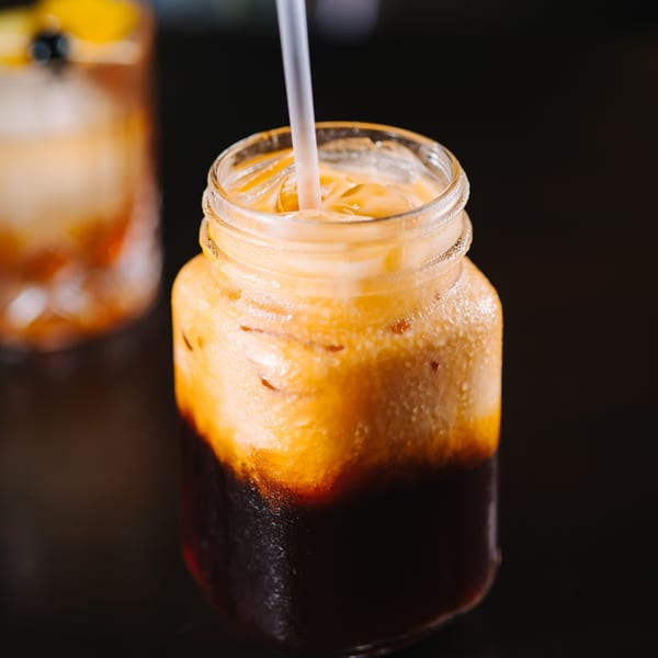 Iced Thai tea in a mason jar with a straw, showing distinct layers of dark tea and creamy milk.