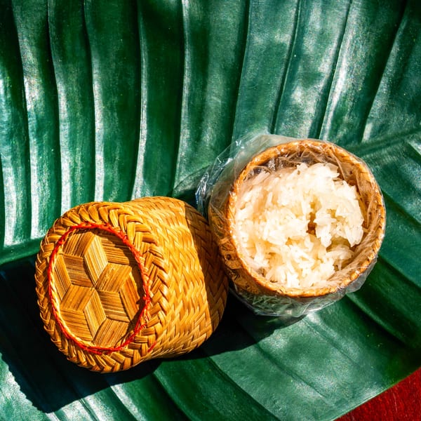 Thai sticky rice in a traditional bamboo basket, with the lid beside it, on a green banana leaf.