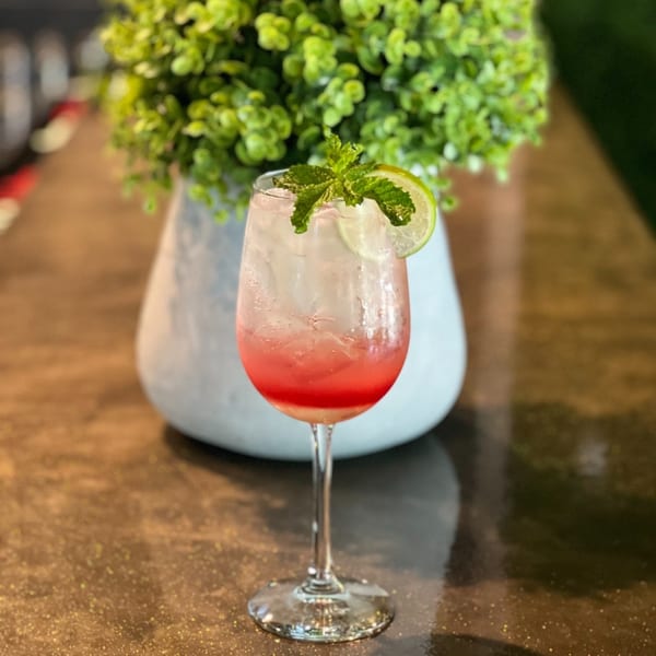A Thailicious cocktail with red liquid, ice, lime, and mint garnish on a dark table.
