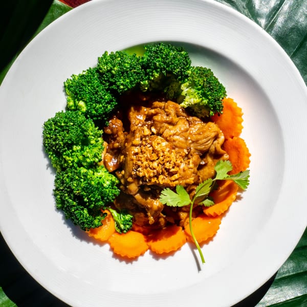 Thailicious's Thai dish with meat in brown sauce, broccoli, carrots, and cilantro on a white plate.