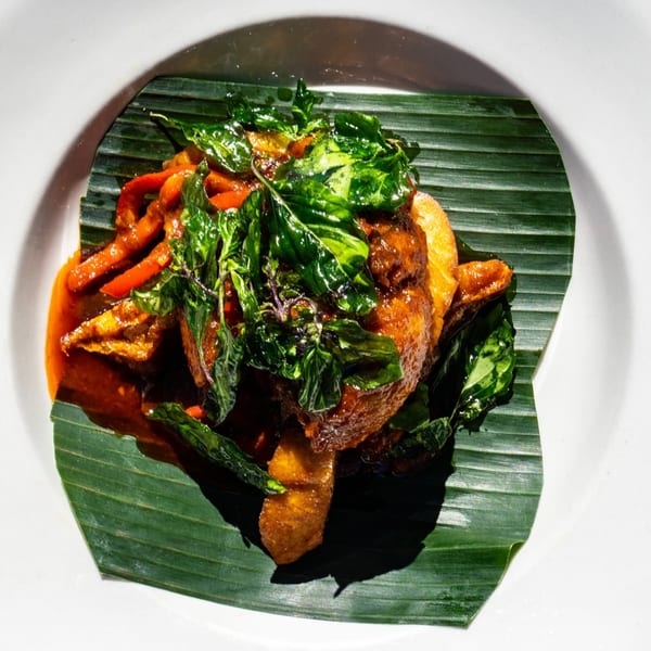 Thailicious' crispy duck with red curry sauce, bell peppers, and basil on a banana leaf.