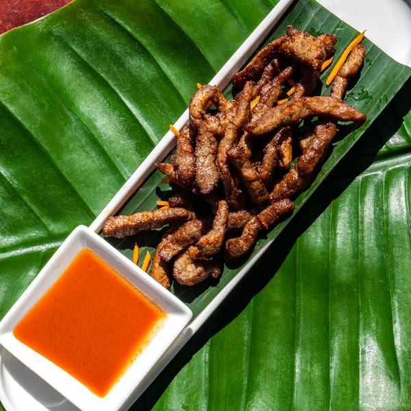 Crispy fried beef strips with a side of orange dipping sauce, served on a banana leaf.